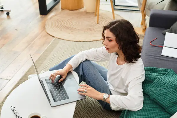 Young woman with curly hair focuses on her laptop while enjoying a cozy workspace at home. — Stock Photo