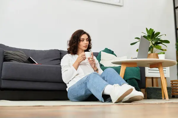 A young woman with curly hair sips her drink, deeply focused on her work in a cozy home setup. — Stock Photo