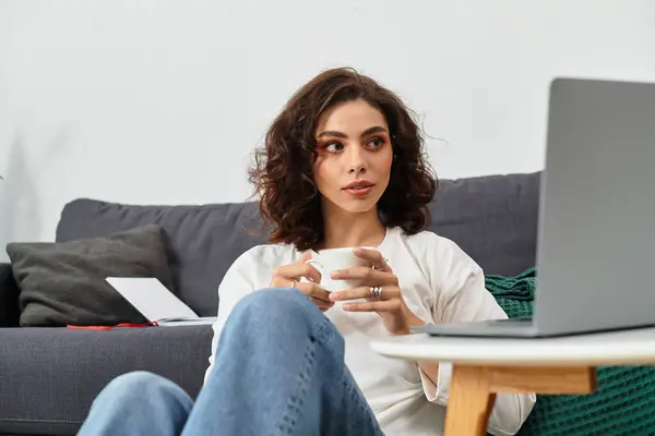 Freelancer sips coffee while focusing on her laptop in a comfortable living space. — Stock Photo