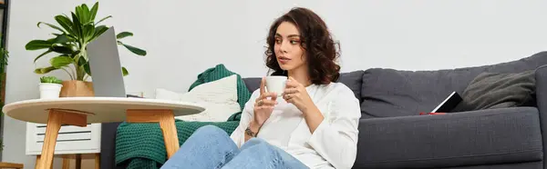 Young woman with curly hair works remotely in a comfortable living room while sipping coffee, banner — Stock Photo