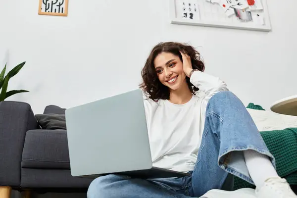 Curly-haired woman smiles while working on her laptop in a relaxed home setting. — Stock Photo