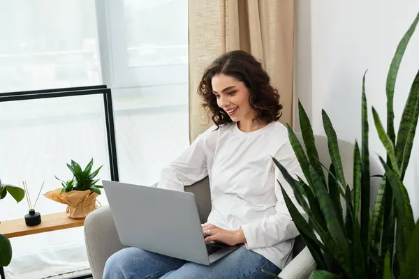 Curly-haired woman focuses on her laptop in a cozy home workspace filled with plants. — Stock Photo