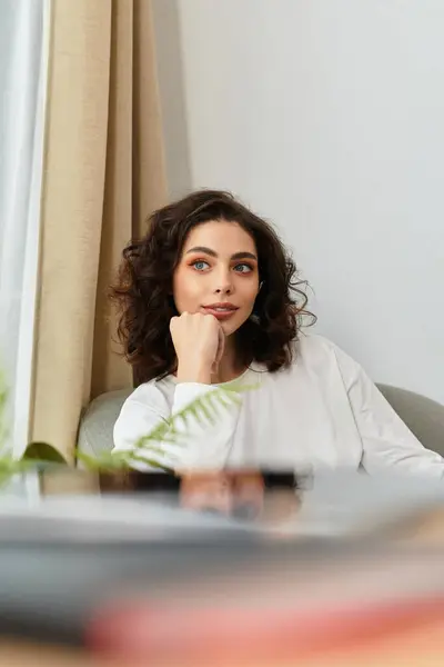 A beautiful young woman with curly brown hair enjoys a moment of rest in her modern apartment. — Stock Photo