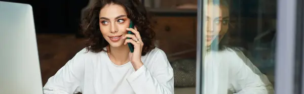 Young woman with curly hair is actively engaged in a phone conversation while working, banner — Stock Photo