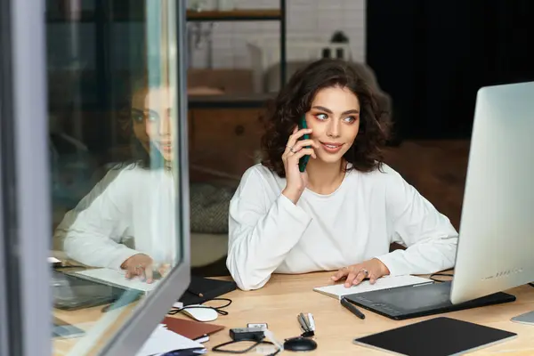 A beautiful young woman edits photos on her graphic tablet while talking on the phone at home. — Stock Photo