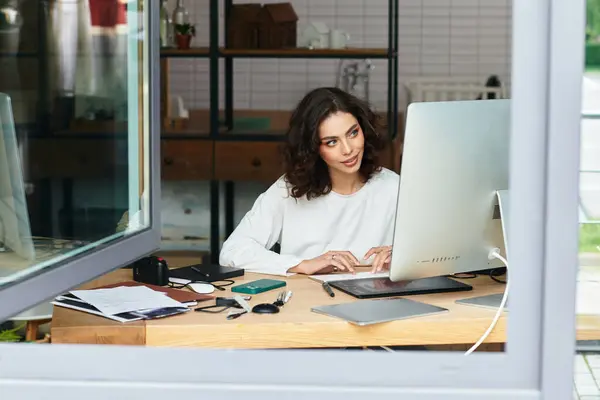 Young woman with curly hair focuses on editing and retouching using a graphic tablet at home. — Stock Photo