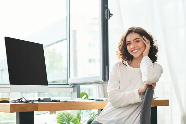 Young woman with curly hair smiles contently while working remotely from her modern home office — Stock Photo