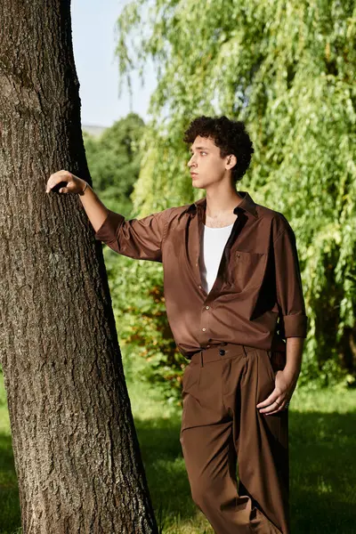 A young man with curly hair relaxes in a lush green park while wearing a trendy summer outfit. — Stock Photo