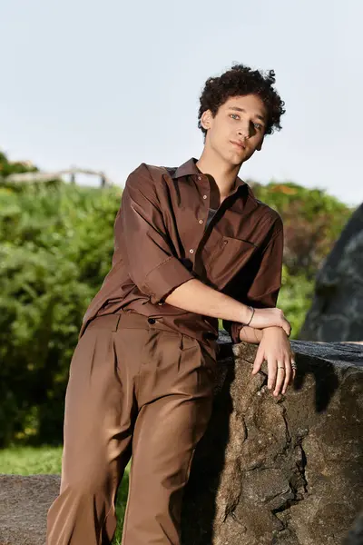 A young man with curly hair relaxes outdoors in a chic summer outfit surrounded by greenery. — Stock Photo