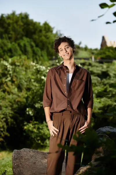 A young man with curly hair sports a trendy summer outfit in a lush park. — Stock Photo