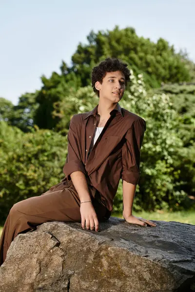 Youthful man in stylish summer attire poses on a rock amidst lush greenery, enjoying nature. — Stock Photo