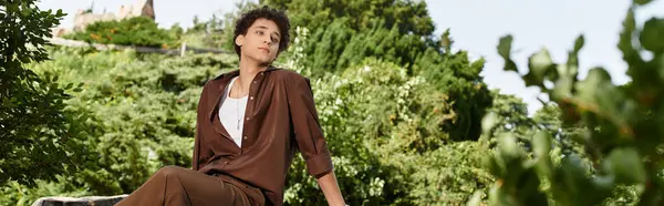 Curly-haired young man relaxes in a vibrant park, showcasing a trendy summer fashion look, banner — Stock Photo