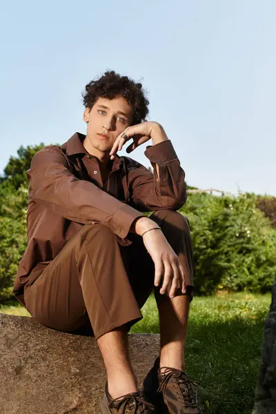 Curly haired young man relaxes on stone while soaking in the warmth of a summer day outdoors. — Stock Photo