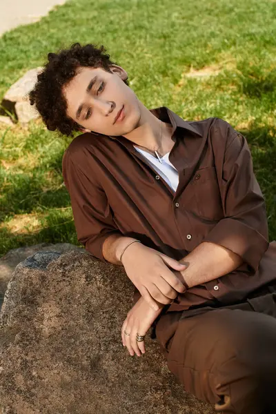 A young man with curly hair enjoys a peaceful moment in a vibrant park, dressed in summer style. — Stock Photo