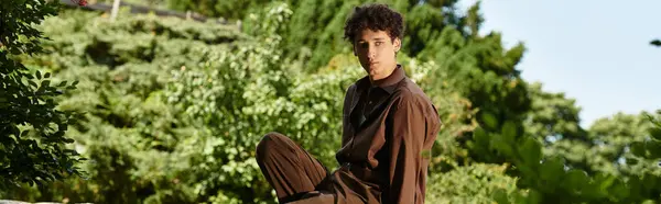 A young man in a trendy summer outfit relaxes in a lush green park, soaking up the sun, banner — Stock Photo