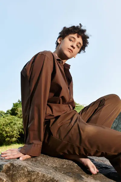 Curly-haired young man relaxes in a park, dressed in a trendy summer outfit under clear skies. — Stock Photo