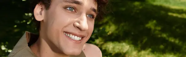 Curly-haired young man relaxes outdoors, embracing vibrant summer fashion in the park, banner — Stock Photo