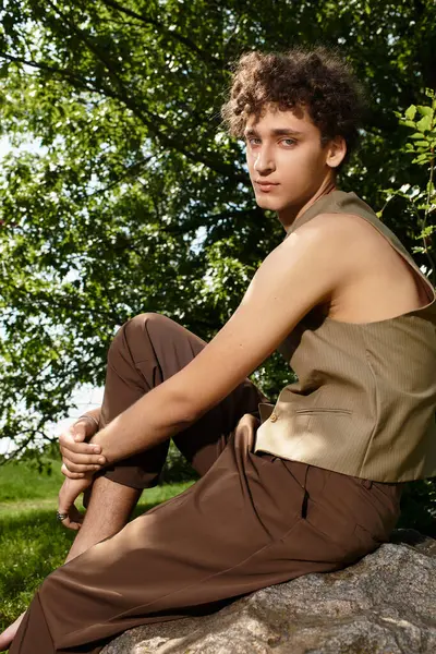 A young man with curly hair relaxes in a park, sporting a trendy summer outfit. — Stock Photo