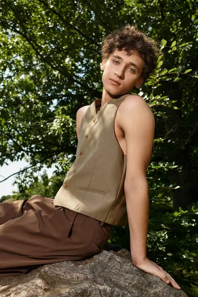 A young man relaxes on a rock in the park, styled in a trendy summer outfit. — Stock Photo