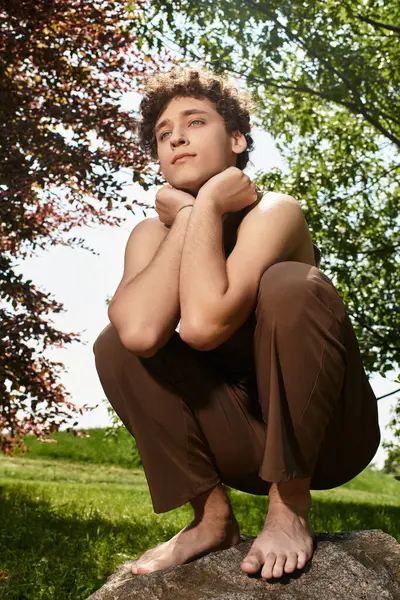 A stylish young man with curly hair relaxes in a lush park, embracing the warm sunlight. — Stock Photo