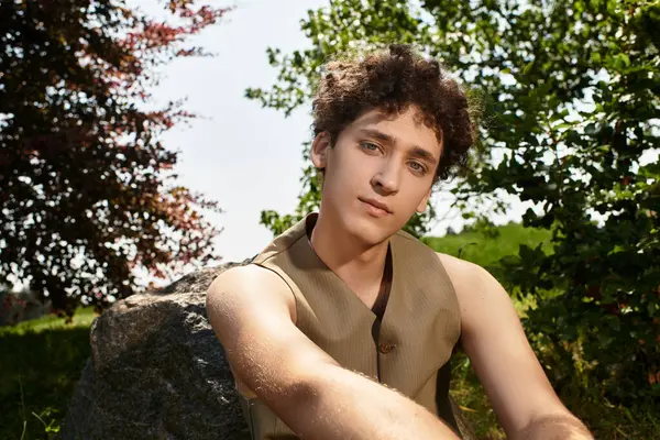 Young man with curly hair relaxes outdoors, showcasing his stylish summer outfit in the park. — Stock Photo