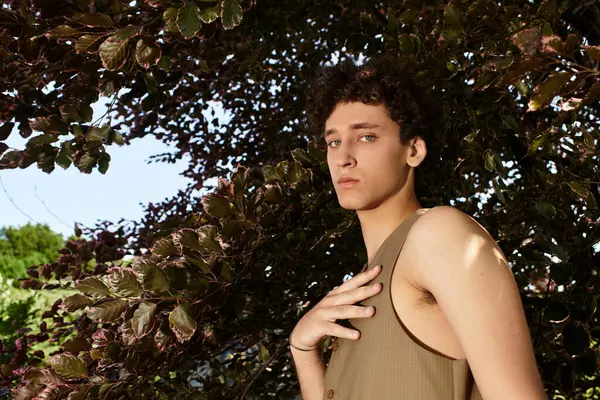 A young man with curly hair showcases his trendy summer outfit in a vibrant green park setting. — Stock Photo