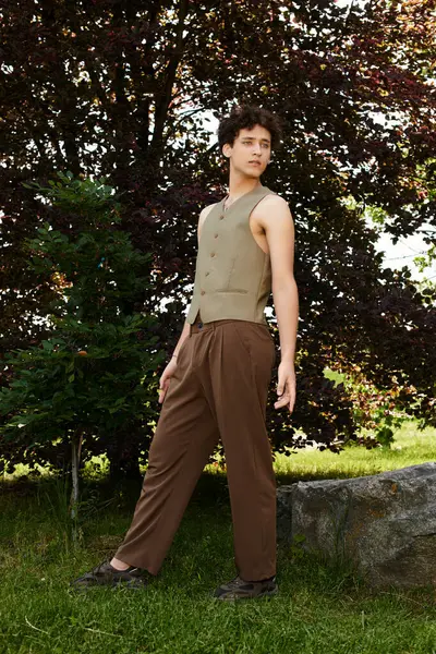 In a lush green park, a young man with curly hair showcases his trendy summer look while relaxing. — Stock Photo