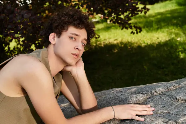 A stylish young man relaxes on a rock, soaking up the warmth of the sunny park. — Stock Photo