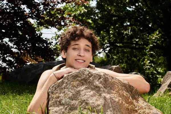 Young man with curly hair relaxes outdoors, embracing the warmth of a sunny summer day in the park. — Stock Photo