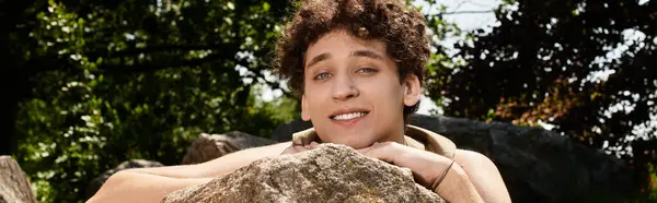 Young man with curly hair relaxes in a green park, dressed in a trendy summer outfit, banner — Stock Photo