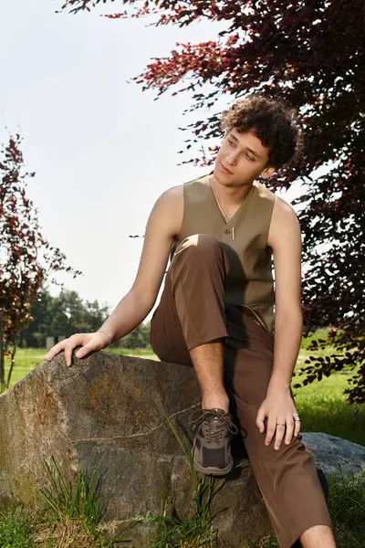 A young man with curly hair relaxes outside in a stylish summer outfit, enjoying nature. — Stock Photo