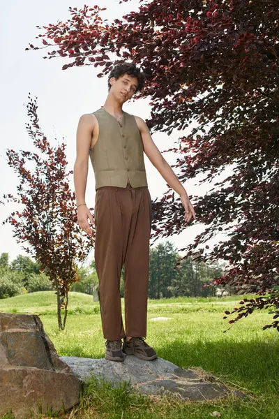 A young man with curly hair relaxes in a green park, sporting a stylish summer outfit. — Stock Photo