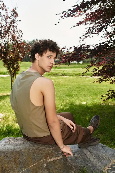 A young man with curly hair relaxes in a vibrant park, soaking up the summer sun in style. — Stock Photo