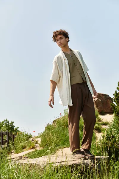 A young man stands confidently in a green park, showcasing his fashion-forward summer outfit. — Stock Photo