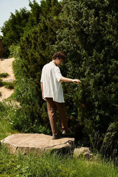 A young man with curly hair explores a serene park while dressed in trendy summer attire. — Stock Photo