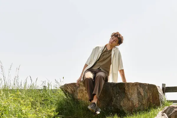 Curly-haired man relaxes on a rock in a green park during a bright summer day, embracing nature. — Stock Photo