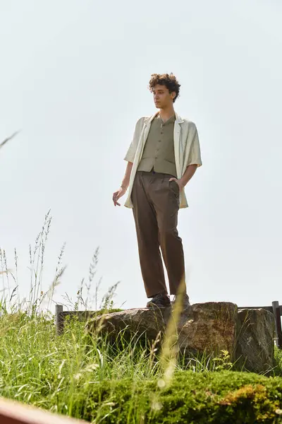 A young man with curly hair wears a trendy outfit while relaxing outdoors in a green park. — Stock Photo