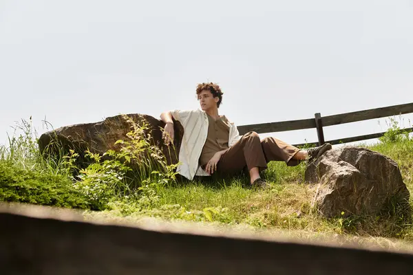 Curly-haired young man enjoys a peaceful moment outdoors in stylish summer attire. — Stock Photo