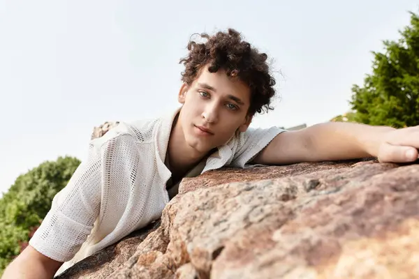 A young man with curly hair relaxes in a picturesque park, embracing the summer vibes. — Stock Photo