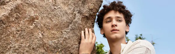 A young man with curly hair enjoys a sunny day in a green park, showcasing his unique fashion sense, banner — Stock Photo