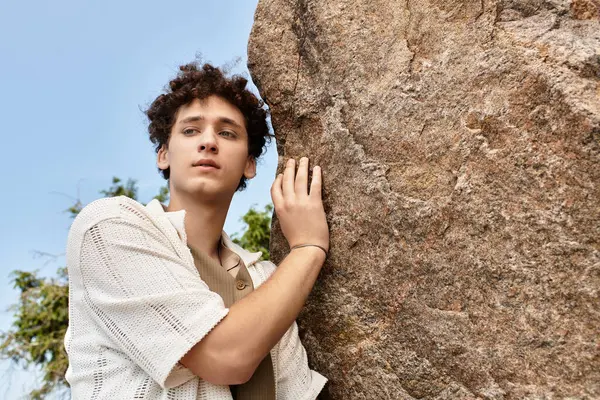 A young man with curly hair relaxes outdoors in a green park, showcasing his summer fashion. — Stock Photo