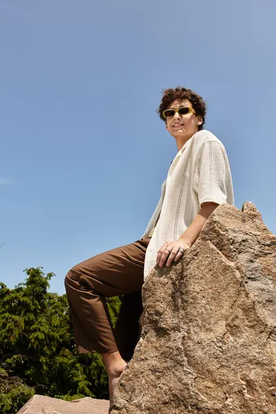 A young man with curly hair relaxes in a vibrant park, showcasing his trendy summer outfit. — Stock Photo