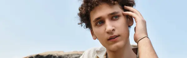 A young man with curly hair relaxes in a lively park, showcasing his fashionable summer look, banner — Stock Photo