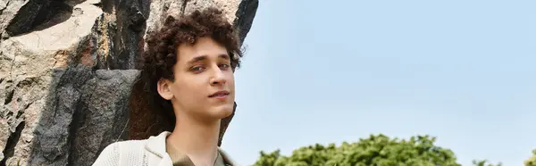 A young man with curly hair relaxes outdoors in a stylish summer outfit surrounded by nature, banner — Stock Photo