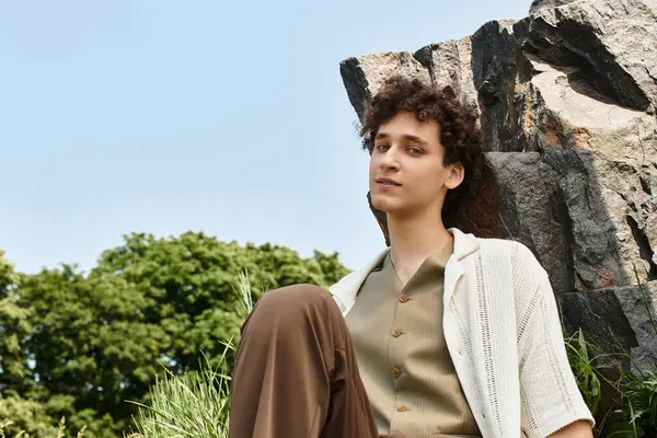 Curly-haired young man relaxes in a park, stylishly dressed for summer amidst nature. — Stock Photo