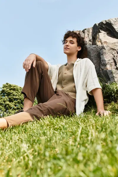 A young man with curly hair relaxes on the grass in a vibrant park, soaking in the sun. — Stock Photo