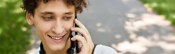 Sunny summer day in the park with a young man in a white t-shirt enjoying a phone conversation, banner — Stock Photo