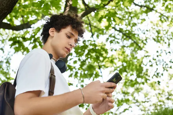 Curly-haired youth relaxes outdoors in a vibrant park while checking his phone. — Stock Photo
