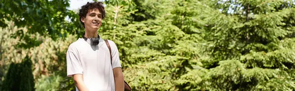 A young man with curly hair relaxes in a vibrant summer park, embracing nature and tranquility, banner — Stock Photo