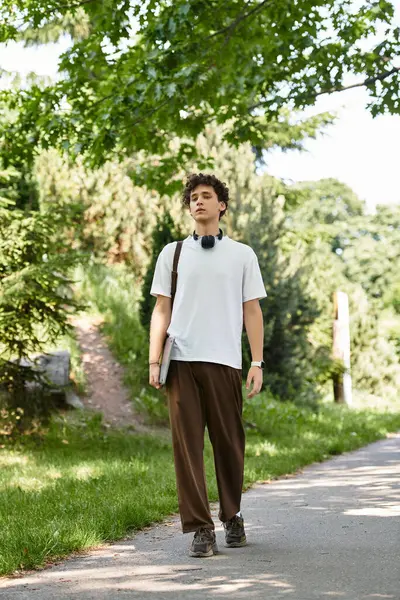 A young man with curly hair strolls through a vibrant green park wearing a white t-shirt. — Stock Photo